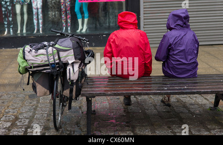 zwei Radfahrer machen Sie eine Pause vom Reiten, sitzen auf einer nassen Bank im Regen in anoraks Stockfoto