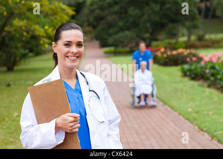 freundliche Ärztin Portrait im Freien ist Hintergrund ihrer Kollegin Patienten im Rollstuhl schieben Stockfoto