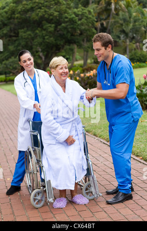 junge Pflege Arzt und Krankenschwester hilft älteren Patienten vom Rollstuhl aufstehen und versuchen, zu Fuß Stockfoto