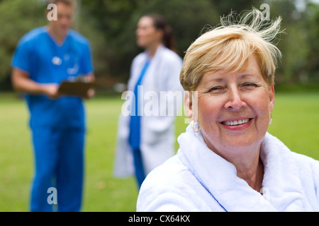 schöne ältere Patienten sitzen auf Rollstuhl im Krankenhaus Garten, Hintergrund ist ihre Ärzte Stockfoto