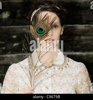 eine Frau mit einem viktorianischen Kleid ist eine Pfauenfeder vor Augen halten. Stockfoto