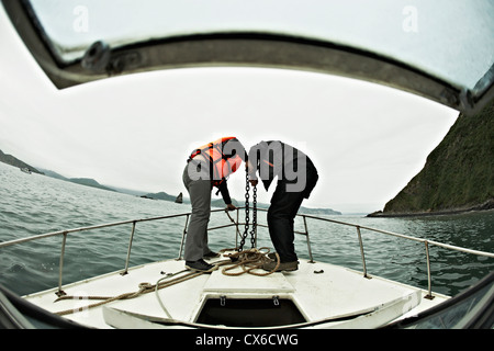 Zwei Menschen engagiert bei der Senkung der Anker aus dem Bug eines Bootes, Awatscha-Bucht, Russland Stockfoto