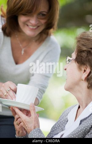 Eine Frau, die Übergabe einer älteren Frau einer Tasse Tee Stockfoto