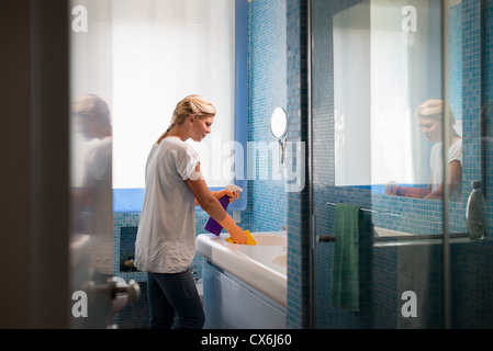 Hausarbeit und inländischen Lifestyle: Frau tun Hausarbeiten im Bad zu Hause, Reinigung Waschbecken und Wasserhahn mit Spray-Reinigungsmittel Stockfoto