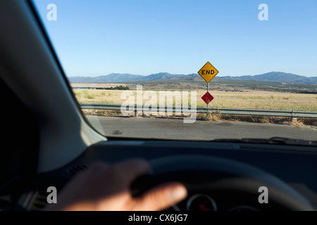 Durch eine Windschutzscheibe ein Ende-Schild und Bergketten hinter anzeigen Stockfoto