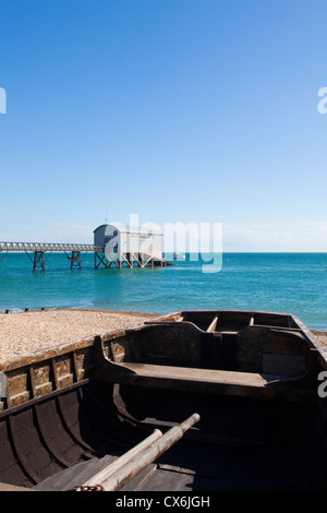 Holz Ruderboot am Strand von Selsey mit Rettungsstation in den Hintergrund, West Sussex, UK. Stockfoto