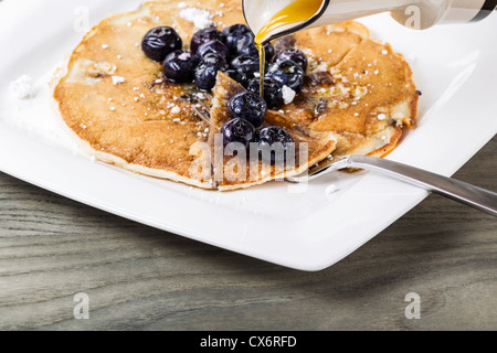 Ahornsirup wird auf frisch gegossen machte Pfannkuchen mit Heidelbeeren an der Spitze Stockfoto