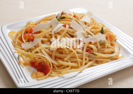 Linguine Pasta warf in einer Sauce aus Olivenöl, Tomaten, Knoblauch und Basilikum und garniert mit Splittern von Parmasan Käse Stockfoto