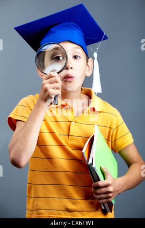 Porträt von neugieriger Junge im Abitur Hut Blick durch die Lupe Stockfoto