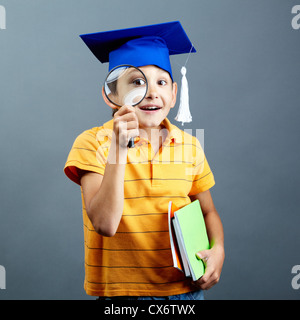 Porträt von neugieriger Junge im Abitur Hut Blick durch die Lupe Stockfoto