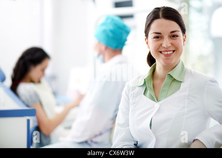 Hübsche Krankenschwester Blick in die Kamera Lächeln auf Hintergrund von Zahnarzt und patient Stockfoto