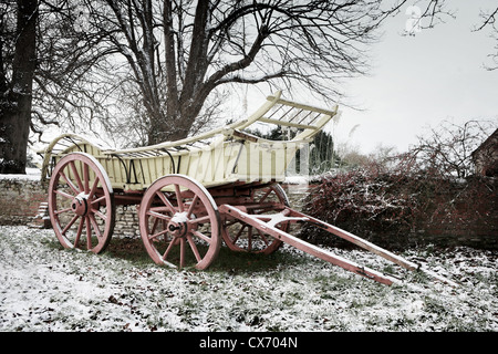 Englische Farm Karren, Pferd gezeichneten Wagen im Schnee in Oxfordshire, England. Die Wiese und die alte Mauer ist frostig und winterlichen. Stockfoto