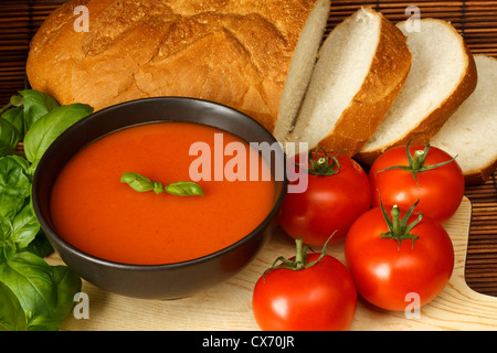 Schüssel mit Tomatensuppe mit Basilikum garnieren, inmitten der Küche umgeben von Zutaten Stockfoto