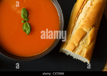 Schüssel mit Tomaten Suppe und Basilikum garniert mit Brot-baguette Stockfoto