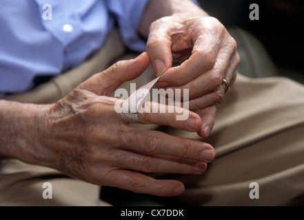 Bandage oder Bandage. Nahaufnahme eines älteren Mannes, der eine Wunde an seinem Finger mit einem Pflaster oder Gips bedeckt. Eine Verletzung zu Hause verkleiden Stockfoto