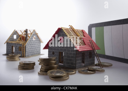 Zwei teilweise gebauten Modelle eines Hauses mit Haufen von Münzen der Europäischen Union um sie herum Stockfoto