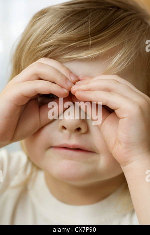 Ein kleines Mädchen durch Gläsern aus den Fingern Stockfoto