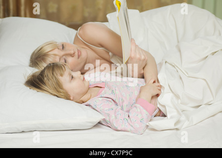 Eine Mutter und ihre kleine Tochter im Bett liegen, ein Buch zu lesen Stockfoto