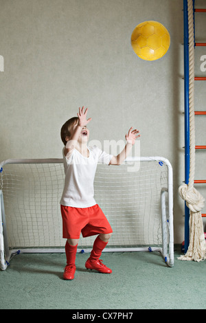 Ein kleiner Junge, ein Tor zu verteidigen, während eine Kugel auf ihn fliegt Stockfoto