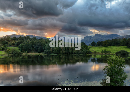 Sonnenuntergang über Langdale Pikes mit loughrigg Tarn Bergsee im Vordergrund, Lake District, Cumbria, Großbritannien Stockfoto