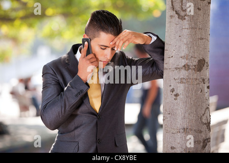 Geschäftsmann mit Problemen bei seinem Handy neben einem Baum sprechen Stockfoto