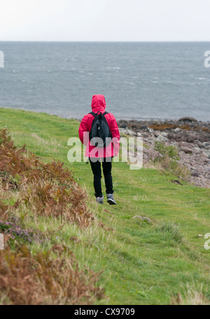 Rückansicht einer Person Frau zu Fuß In den Regen trägt eine rote Regenjacke mit Kapuze Stockfoto