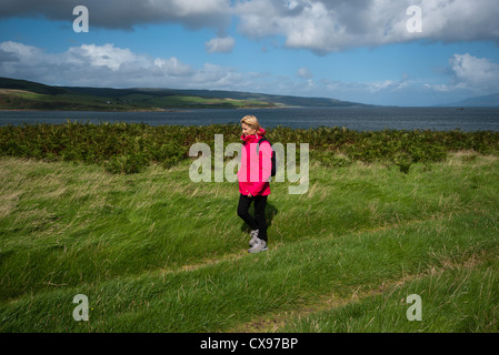 Seitenansicht einer Frau Person zu Fuß durch die Landschaft tragen wasserdichte Kleidung und Rucksack Stockfoto