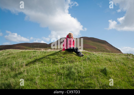 Vorderansicht einer Frau Rambler Walker Person sitzen auf dem Rasen auf dem Lande, wasserdichten Kleidung tragen Stockfoto