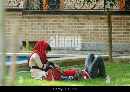 Ein junger Mann liegt auf dem Gras, während eine junge Frau mit rotem Hijab neben ihm in einem Park in Teheran, Iran, sitzt Stockfoto