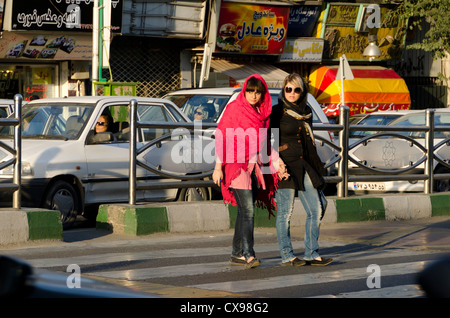 Zwei junge Damen mit westlicher Kleidung und obligatorischem islamischem Hijab überqueren die Straße an einer Fußgängerbrücke in Tajrish, Nord-Teheran, Iran. Stockfoto