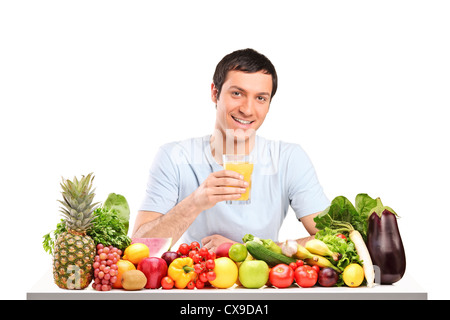 Hübscher Kerl mit Glas Orangensaft, auf einem Tisch voller Obst und Gemüse isoliert auf weißem Hintergrund Stockfoto