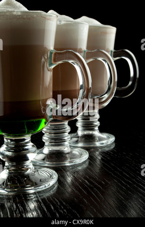 Eine Gruppe von drei Gläser heiß geschichteten alkoholische Cocktails, dekoriert mit Milchschaum auf schwarzen Tresen Stockfoto