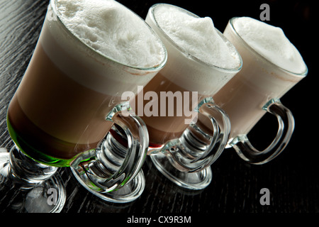 Eine Gruppe von drei Gläser heiß geschichteten alkoholische Cocktails, dekoriert mit Milchschaum auf schwarzen Tresen Stockfoto