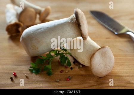 Rohe König Trompete Pilze, Pfeffer, Petersilie und Kochmesser auf Holztisch Stockfoto