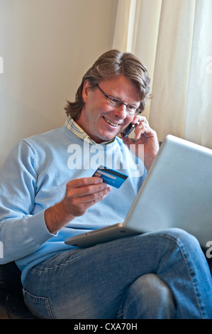 Reifer Mann zu Hause, eine finanzielle Transaktion zu verdienen online mit seinem Laptop und ein iPhone 4 s-smartphone Stockfoto