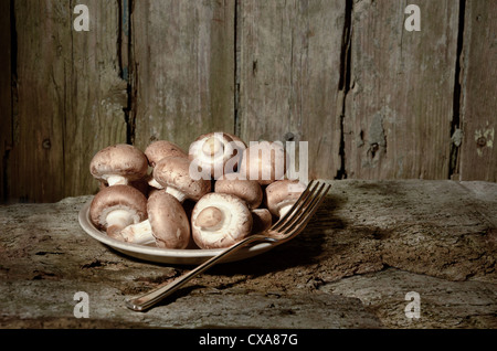 Bio Pilze produzieren braune Champignons roh in einem Teller bereit mit Gabel bereit, alte Tisch gegessen Nahrung gekocht werden abgeholt Stockfoto