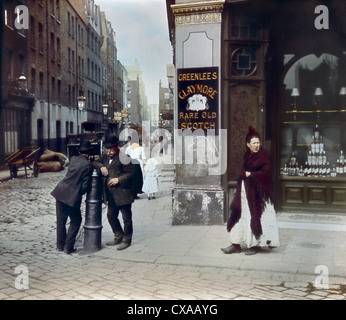 Eingefärbtes Foto von Leuten außerhalb eines East End Pubs, London, England, 1895. Zwei Männer lehnen sich an einen Pfosten an der Straßenecke. Ein Schild für ‘Greenlees Claymore Rare Old Scotch’ ist vor dem Pub ausgestellt. (Foto von Burton Holmes) Stockfoto