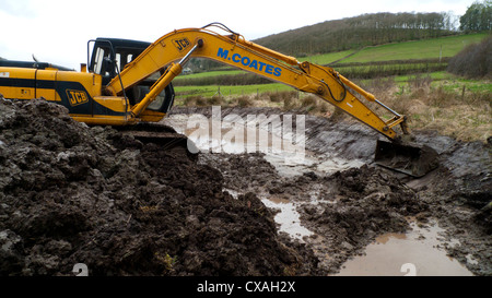 Auftragnehmer mit einem 360-Grad-Bagger graben Teich Tiere auf einem Bauernhof. Powys, Wales. April Stockfoto