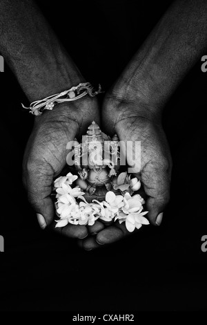 Hinduistische Elefantengott. Indische mans Hand mit Lord Ganesha Statue und Jasminblüten auf schwarzem Hintergrund. Monochrom Stockfoto