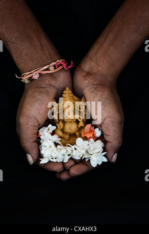 Hinduistische Elefantengott. Indische mans Hand mit Lord Ganesha Statue und Jasminblüten vor schwarzem Hintergrund Stockfoto