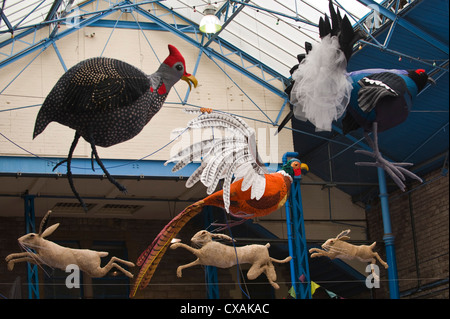 Kunstinstallation von Federwild und springenden Hasen hängen vom Dach der Markthalle in Abergavenny Food Festival Stockfoto