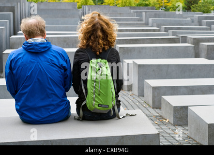 Zwei Touristen sitzen auf einem von Betonsteinen, aus denen sich das Holocaust-Mahnmal in Berlin, Deutschland Stockfoto