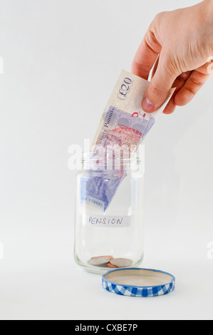 Eine Hand, ein Glas mit "Rente" Label eine £20-Pfund-Note hinzufügen. Stockfoto