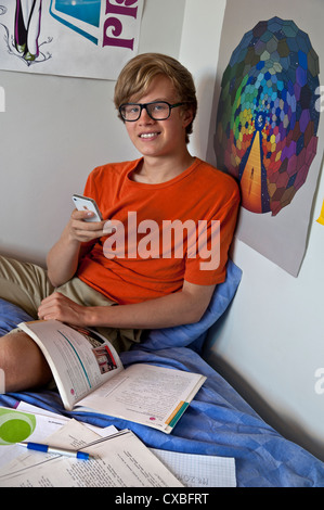 Entspannte fleißig Teenager SMS mit seinem iPhone Smartphone in seinem Schlafzimmer während Schule Hausaufgaben Studien Stockfoto