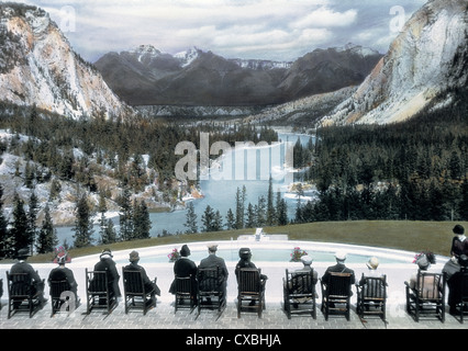 Koloriertes Foto von Touristen, die in Stühlen auf einer Terrasse mit Blick auf einen Swimmingpool und einen malerischen Blick auf das Bow River Valley sitzen, Banff Springs Hotel, Banff, Kanada, 1916. (Foto von Burton Holmes) Stockfoto