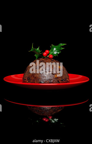 Foto von einem traditionellen Christmas Pudding mit Holly und Beeren an der Spitze, auf einem schwarzen Hintergrund. Stockfoto