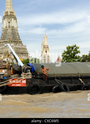 Mann auf Boot am Chao Phraya-Fluss mit Wat Arun (Tempel der Morgenröte) im Hintergrund Stockfoto