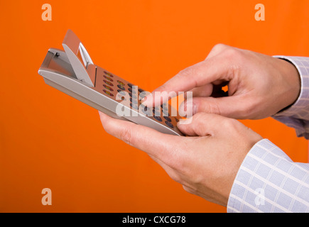 Hand mit einem Taschenrechner isoliert auf einem orangefarbenen Hintergrund Stockfoto