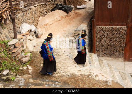 Miao-Frauen in traditioneller Kleidung gehen durch eine steingepflasterte Gasse, Xijiang, China Stockfoto