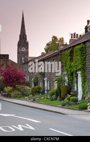 Terrasse Zeile aus Stein gebauten Cottages am Straßenrand mit hoch aufragenden Turm & Uhr der St. Mary's Kirche jenseits - Burley-in-Wharfedale, Yorkshire, England, UK. Stockfoto